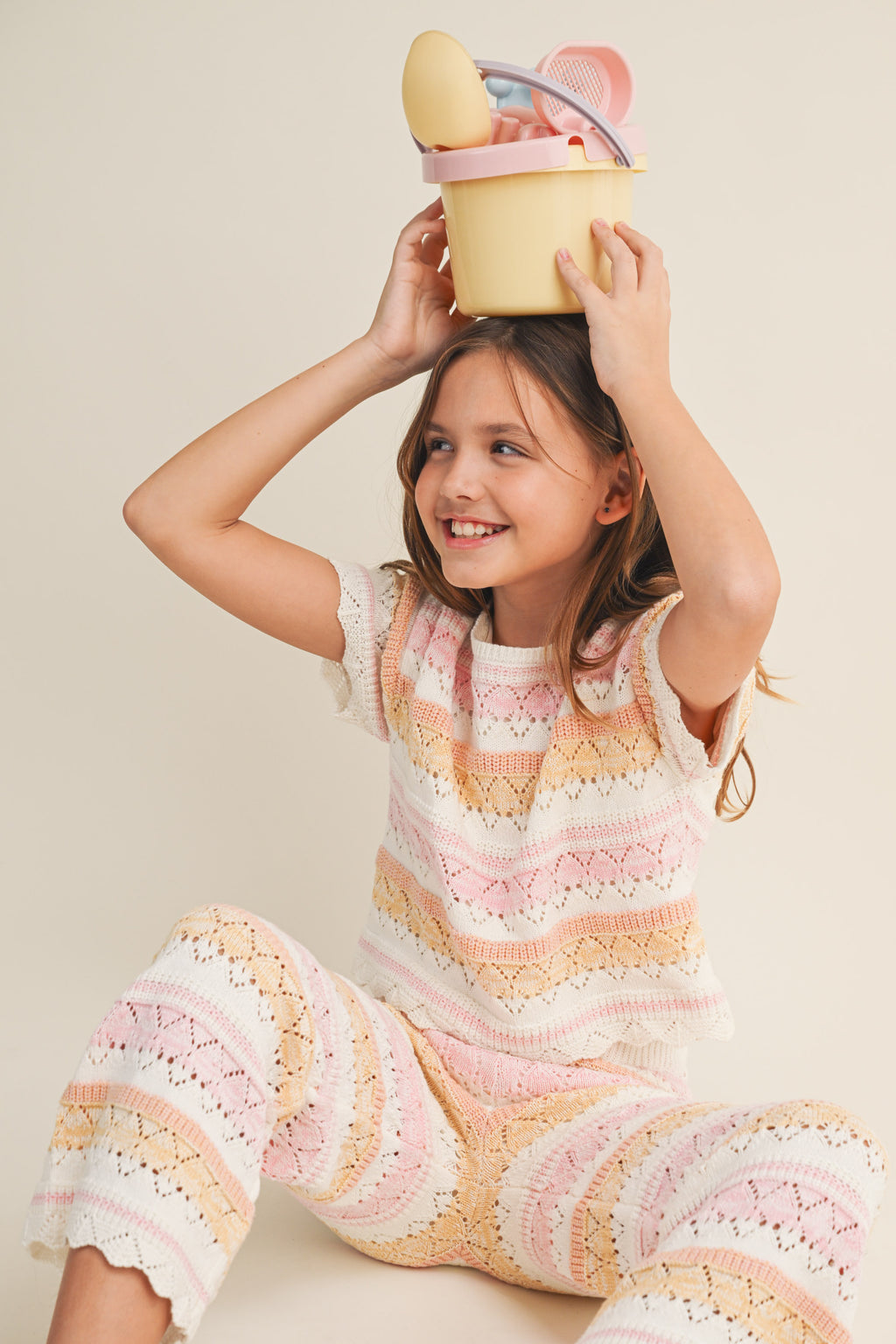 Young girl in a striped outfit holding a yellow bucket with a toy inside.